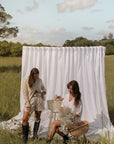 Two models wearing POŚI linen outfits holding white flowers in a farm setting – capsule country-luxe fashion from Australia
